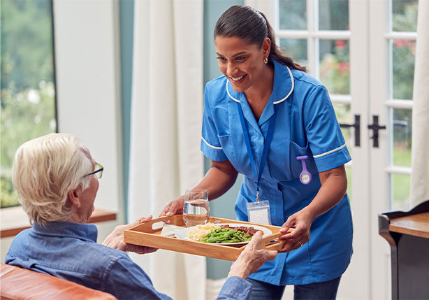Female care worker bringing meal to an elderly man